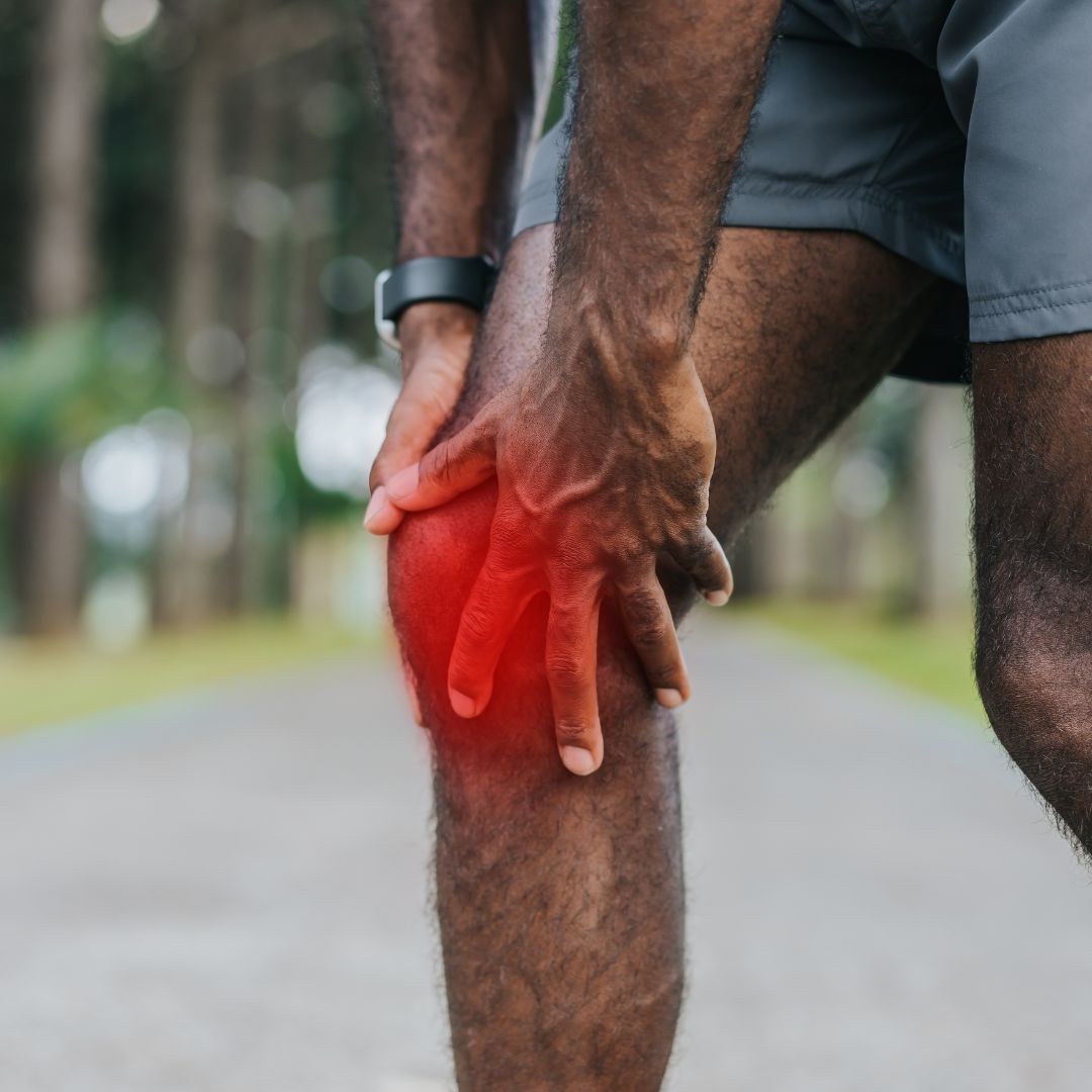 Runner holding the front of the knee with pain highlighted below the kneecap, typical of patellar tendinopathy or jumper’s knee